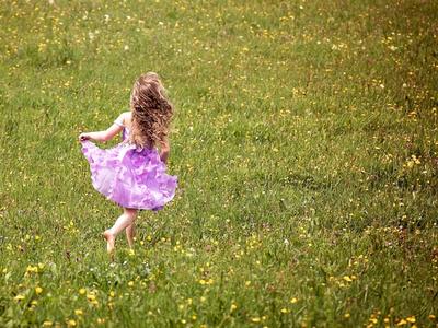 Bild vergrößern: Ausgelassen: Ein kleines Mädchen mit langem blonden Haar und rosa Rüschenkleidchen flitzt barfuß über eine Blumenwiese.