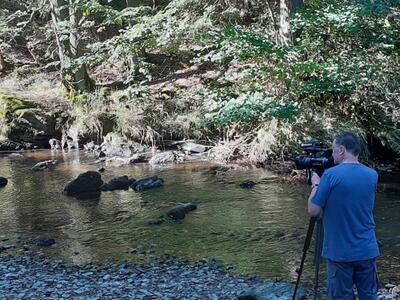 Bild vergrößern: Kameramann mit Kamera der Filmaufnahmen im Fluss macht.